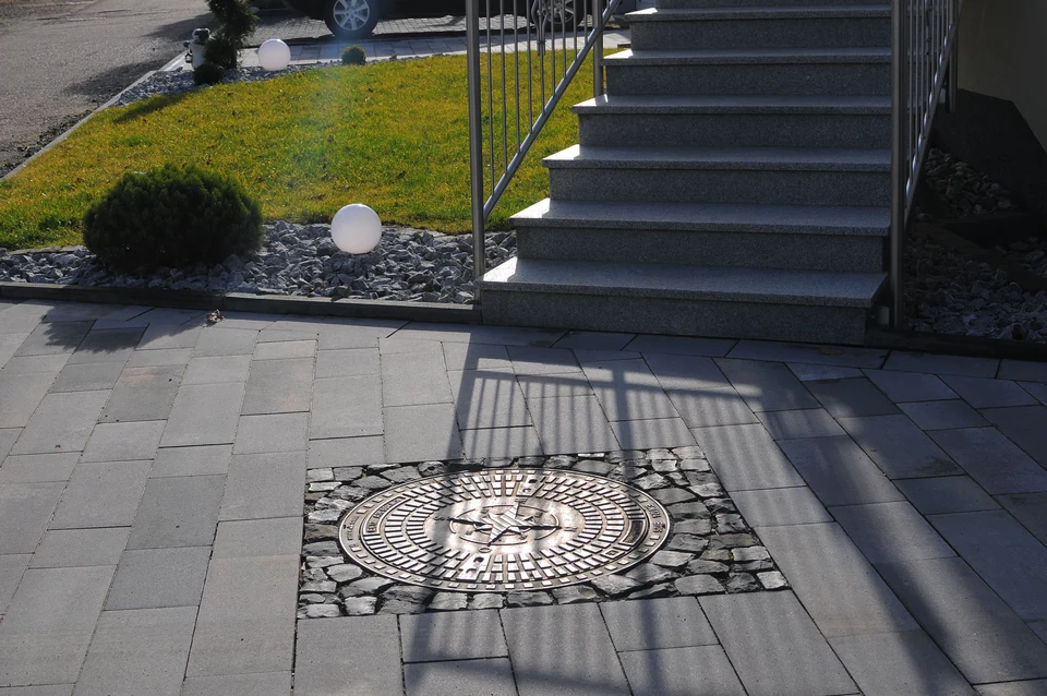 Pflasterfläche mit Natursteineinsatz und Treppe zum bepflanzten Garten