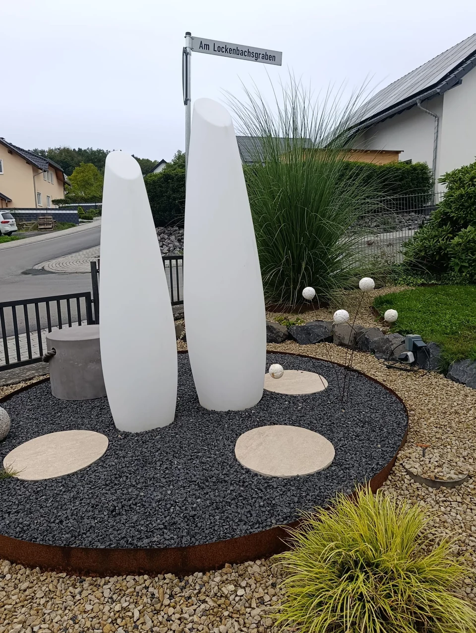 Gestaltetes Kiesbeet mit Trittplatten, Gräsern und weißen Gartenelementen