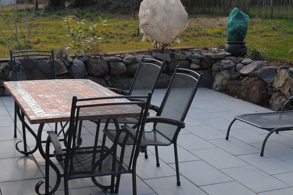 Gepflasterter Sitzplatz vor einer Natursteinmauer und Rasenfläche