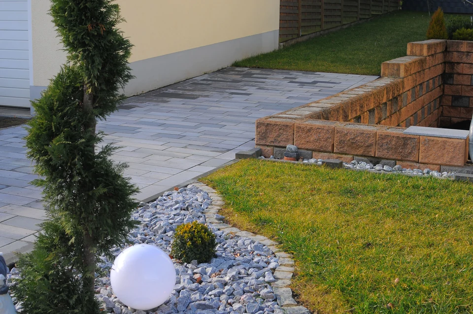 Formgeschnittenes Gehölz zwischen Steinbeet, Rasen und Pflasterweg
